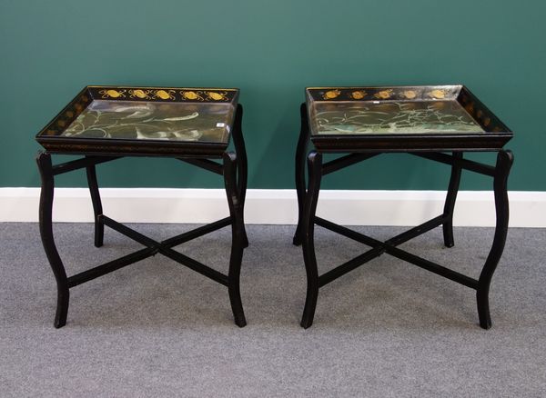 A pair of early 20th century black lacquer chinoiserie decorated square trays on folding stands, 54cm wide.