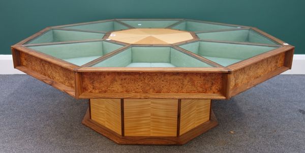 A 20th century sycamore, burr yew and walnut octagonal coffee/display table, the top with eight glazed top compartments on column base, 118cm wide.