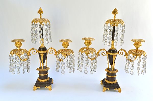 A pair of William IV gilt and patinated bronze twin light candelabra, circa 1830, hung overall with cut glass drops on lion mask paw feet, 46cm high.