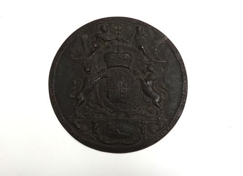 A bronze circular plaque, early 19th century, relief cast with the English Royal standard within a Latin script border, 17.5cm diameter.