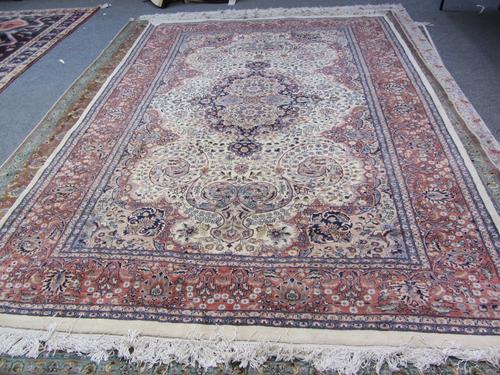 An Indian carpet, the ivory field with a fawn and indigo medallion, matching spandrels, all with intricate floral sprays, a brown palmette and vine bo