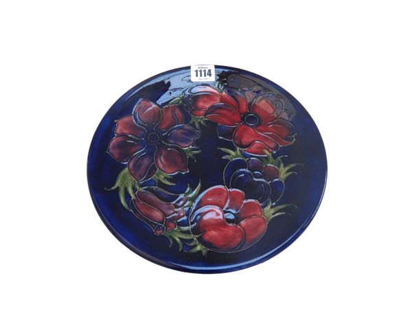 A Moorcroft pottery plate decorated with anemone against a blue ground, painted and impressed marks, 25.7cm diameter.