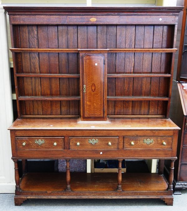 An inlaid George III oak dresser, the enclosed three tier plate rack with central spice cupboard over three frieze drawers on baluster turned supports