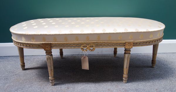 A Louis XVI style footstool, the rounded rectangular top on six grey painted parcel gilt tapering supports, 120cm wide.