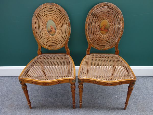 A pair of Sheraton Revival painted satinwood and cane work open armchairs with serpentine seat on turned supports, together with a similar pair of sin