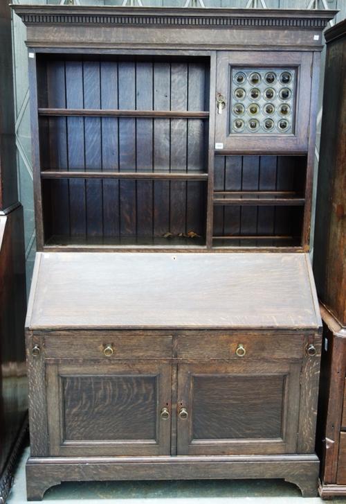 Liberty & Co, an early 20th century oak bureau bookcase, the upper section with open tiered shelves and single door with leaded bullseye glazing, the