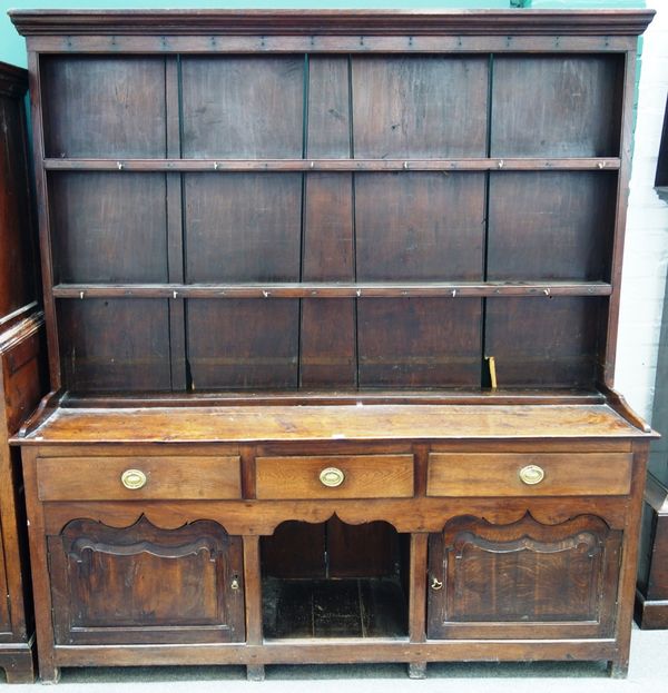An 18th century and later oak dresser, the enclosed three tier plate rack over three frieze drawers, central recess and pair of shaped panelled cupboa