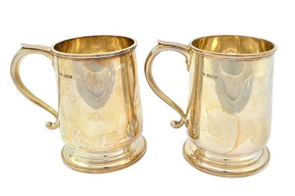 A pair of silver mugs, each of tapered cylindrical form, with a scrolling handle and raised on a circular foot, in the 18th century taste, Sheffield 1