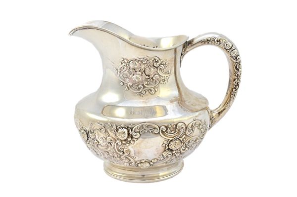 A Sterling silver jug, probably American or Canadian, of oval baluster form, with floral, foliate and scroll embossed decoration, on a plain oval foot