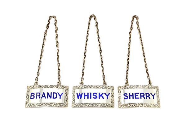 A set of three silver and blue enamel decanter labels detailed 'Whisky', 'Brandy' and 'Sherry', with engraved scroll borders by Turner and Simpson, Bi