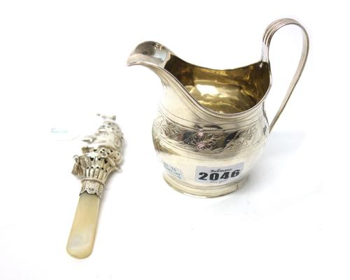 A George III silver helmet shaped milk jug, decorated with an engraved foliate band, London 1802 and a silver baby's rattle, formed as the head of Mr