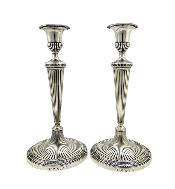 A pair of George III silver table candlesticks, each column of tapered form having fluted decoration and on swept circular bases with fluted decoratio