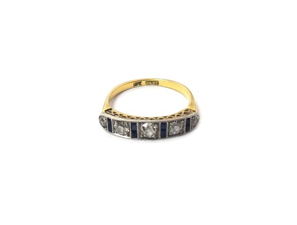 A gold and platinum ring, mounted with a row of five cushion shaped diamonds, graduating in size to the centre stone and with four pairs of calibre cu