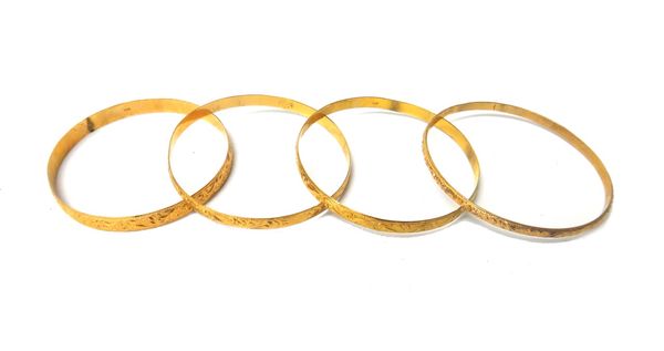 Four circular gold bangles, each with scroll engraved decoration, mostly detailed 18 K, (some marks indistinct), combined weight 46.5 gms.