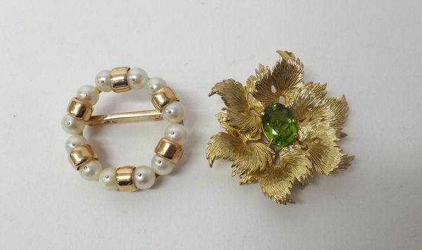 A peridot set single stone brooch in a hexagonal foliate design, mounted with an oval cut peridot, with a textured finish and a cultured pearl mounted