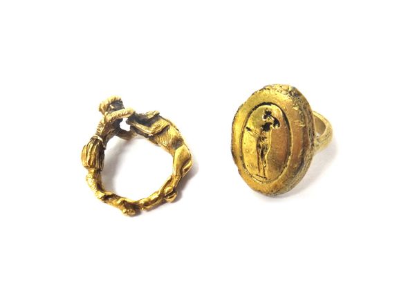 A gold copy of an antiquity oval signet ring, detailed with a standing figure motif, ring size J and a half and a gold ring, formed as an Eastern figu