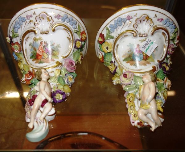 A pair of ceramic wall shelves moulded with cherubs and flowers. (2)