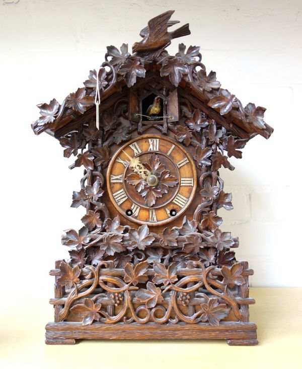 A Black Forest carved walnut or Linden wood mantel clock, late 19th century, with automaton cuckoo within an ornately carved foliate case in the manne
