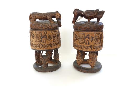 A pair of carved wooden covered pots, Grasslands style, Cameroon, each with relief carved band of birds, raised on carved mask legs, the removable cov
