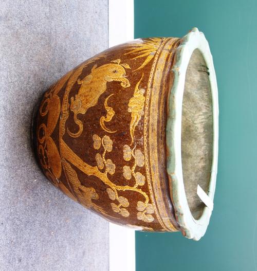 An Asian glazed stoneware jardiniere, 20th century, with foliate rim decorated with mythical beasts, birds and bats in ochre against a brown ground; t
