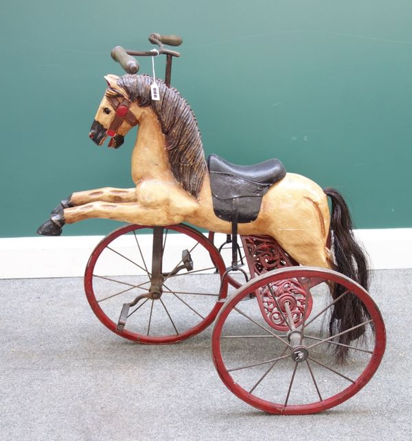 A reproduction horse tricycle (velocipede), of polychrome painted carved wood with faux leather saddle and wrought iron framework (a.f), 81cm high.