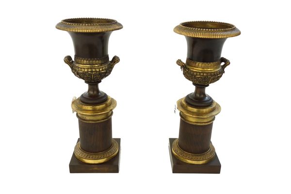 A pair of Empire style bronze and gilt brass mounted campagna urns, late 19th century, on ribbed cylindrical socles and square bases, 30cm high. (2)