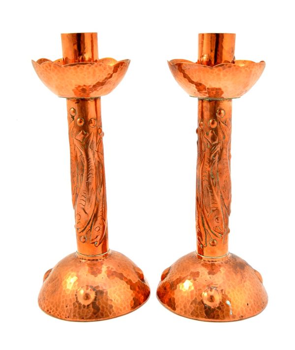 A pair of Newlyn copper candlesticks, each with embossed fish decoration over a domed foot, with a beaten finish, stamped 'Newlyn', 21cm high. (2)  Il