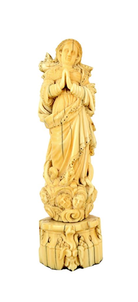 A Goan ivory carving of the Madonna, 19th century, in a contemplative pose above winged angelic masks and a serpent, on a shaped ivory plinth, 18.5cm