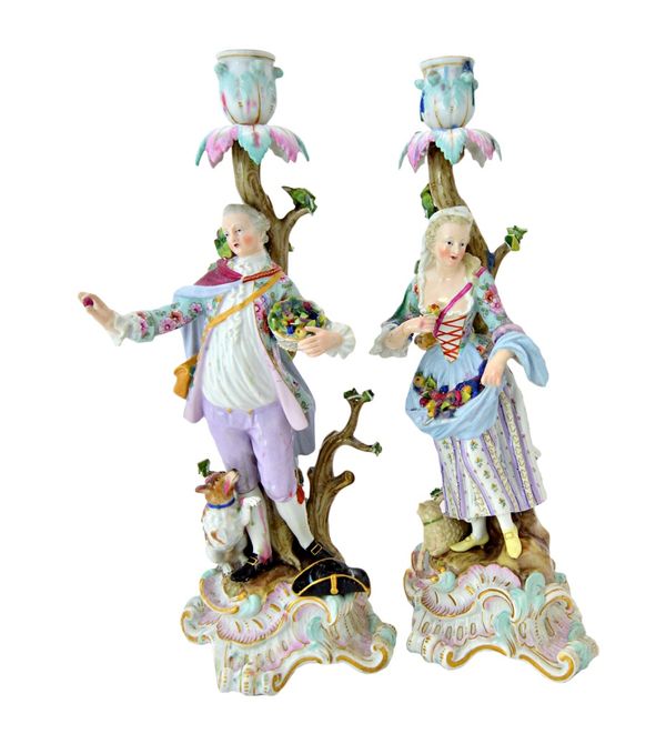 A pair of Meissen porcelain figural candlesticks, late 19th century, each modelled as a gallant and companion, holding fruit with a dog or sheep at th