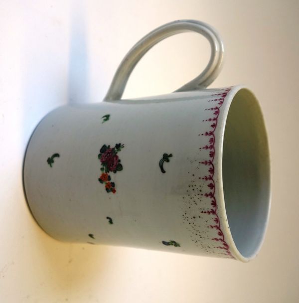 A Plymouth  porcelain cylindrical mug, circa 1770, set with ribbed handle and painted with a flower spray and scattered sprigs beneath a puce border,