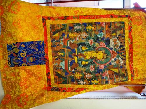 A Tibetan thangka, late 19th/early 20th century, pigment on cloth, painted in the centre with a seated Buddha, surrounded by flowers, further deities