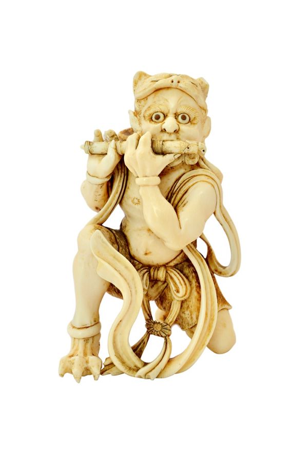 A Japanese ivory okimono of an oni, Meiji period, carved kneeling playing a flute, a tiger pelt over his head, 10cm. high. Illustrated.