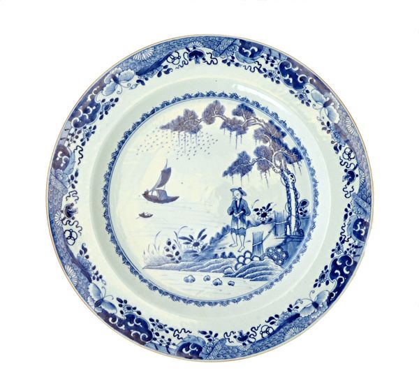 A large Chinese export blue and white dish, 18th century, painted with a figure standing beneath a pine tree on the banks of a river, within an elabor
