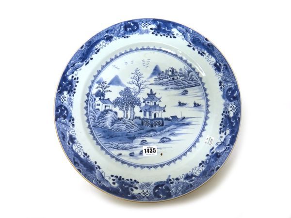 A large Chinese export porcelain blue and white dish, 18th century, painted with a central river landscape inside an elaborate border painted with ins