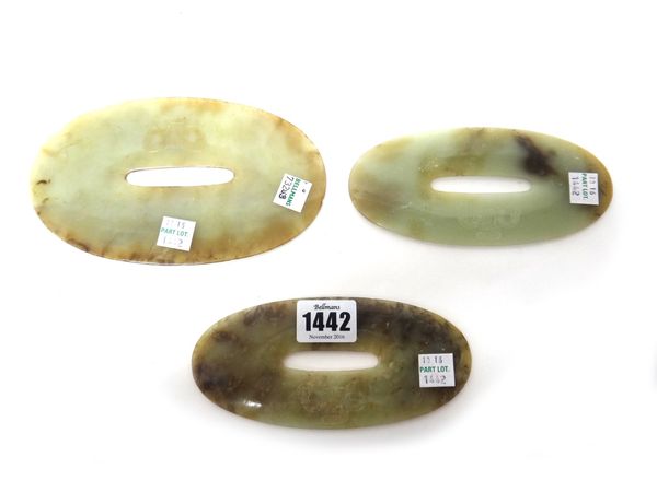 Three Chinese green and brown jade graduated oval pierced discs, each carved with a mask, 14cm. to 17cm. wide.