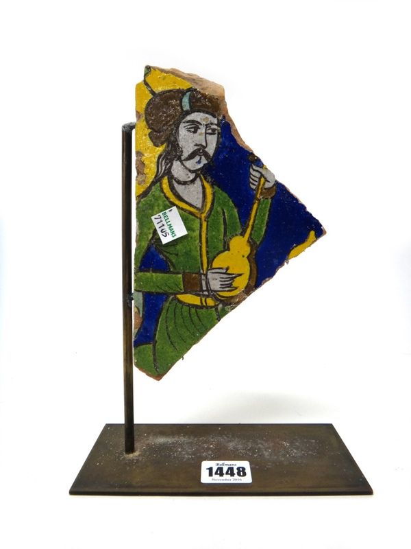 A Persian pottery tile fragment, 19th century, painted with a man playing a musical instrument, (a.f), 20cm. high by 11.5cm. at widest point.