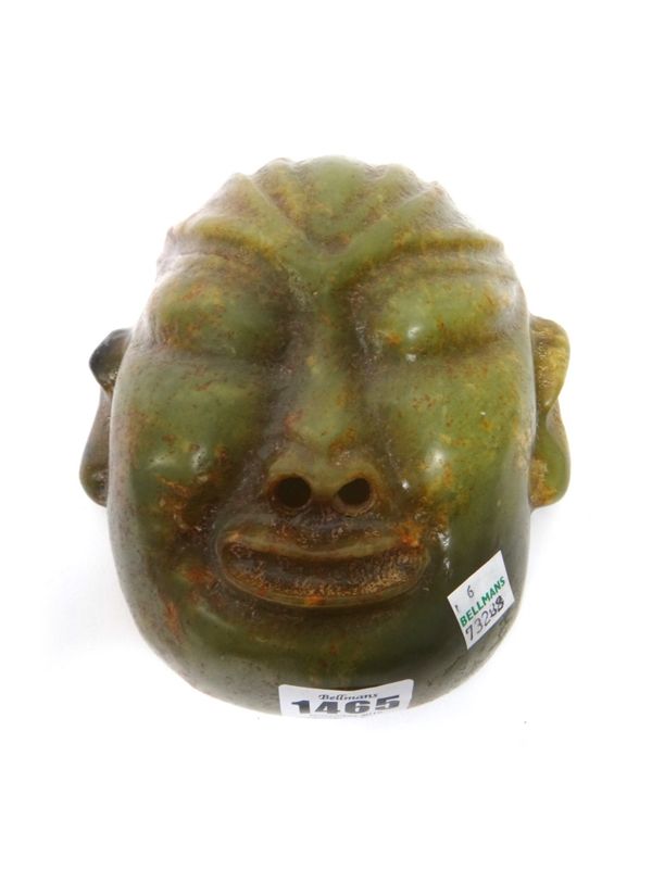 A Chinese jade mask of Buddha, the stone of green colour with russet and grey inclusions, the nostrils pierced, 16cm.high.