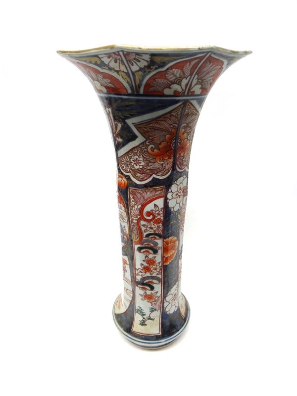 A tall Japanese Imari beaker vase, Edo period, circa 1700, painted in underglaze blue, iron-red, green and gilt with a panel of pavilions in a landsca
