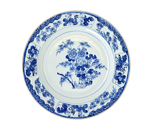 A large Chinese export porcelain blue and white dish, Kangxi, painted in the centre with chrysanthemum, bamboo and lotus, inside a border reserved wit