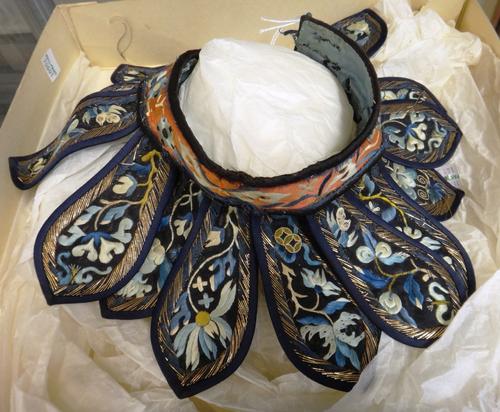 A Chinese embroidered collar, circa 1900, the red ground collar suspended with fifteen blue bordered black ground lappets embroidered with flowers, bi