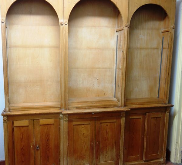 An 18th century design pine breakfront bookcase cupboard, with pair of arch top open shelves over six cupboards, 219cm wide x 223cm high.