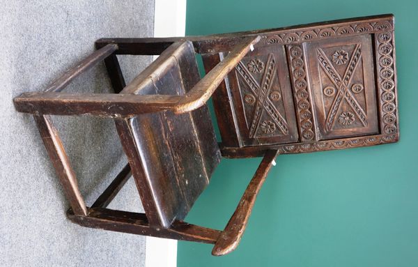 A 17th century later oak open armchair, with carved double panel back on solid seat and block supports.