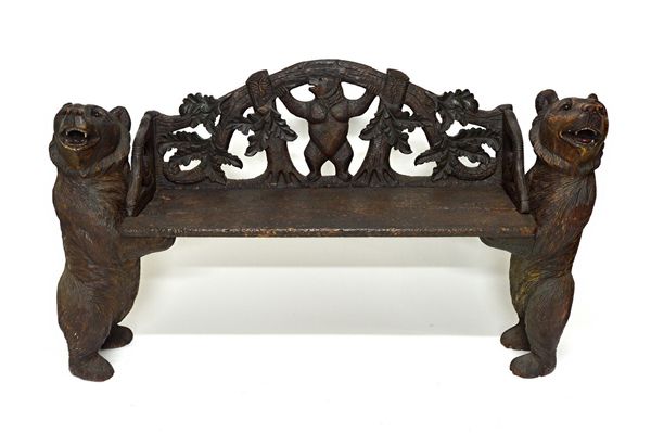 A 19th century Black Forest style carved wood bench, the pierced back depicting a bear amongst foliage over solid seat, on a pair of standing bear sup