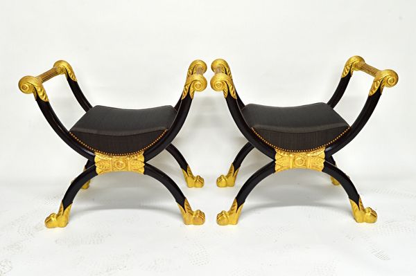 A pair of Egyptian Revival ebonised and gilt mounted 'X' frame stools, on paw feet, 82cm wide (2). Illustrated.