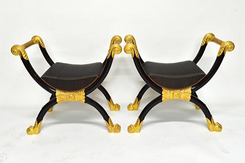 A pair of Egyptian Revival ebonised and gilt mounted 'X' frame stools, on paw feet, 82cm wide (2). Illustrated.