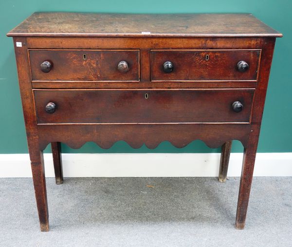 An 18th century oak side cabinet with two short over one long drawer, above shaped frieze on tapering square supports, 99cm wide.