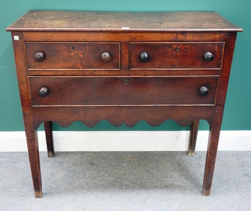 An 18th century oak side cabinet with two short over one long drawer, above shaped frieze on tapering square supports, 99cm wide.