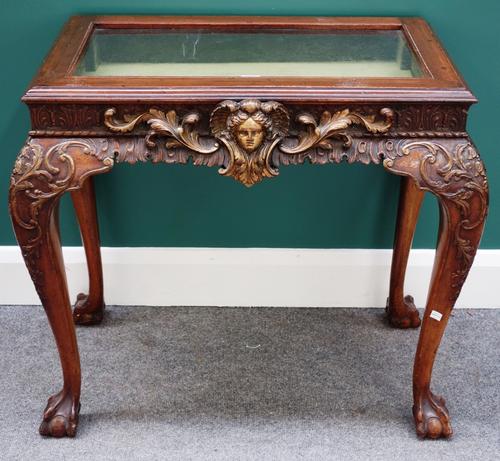An early 20th century bijouterie table of 18th century design, the glazed lift top over a carved frieze, centred with a face mask on cabriole supports