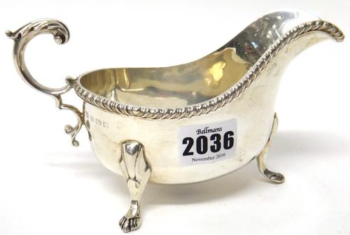 A silver sauceboat, with a decorated scrolling handle, gadrooned rim and raised on three feet, Birmingham 1935, weight 316 gms.