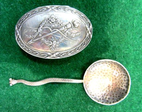 A European oval hinge lidded box, the cover decorated with a bow and floral scrolls, gilt within and a spoon, with a serpentine handle, probably India